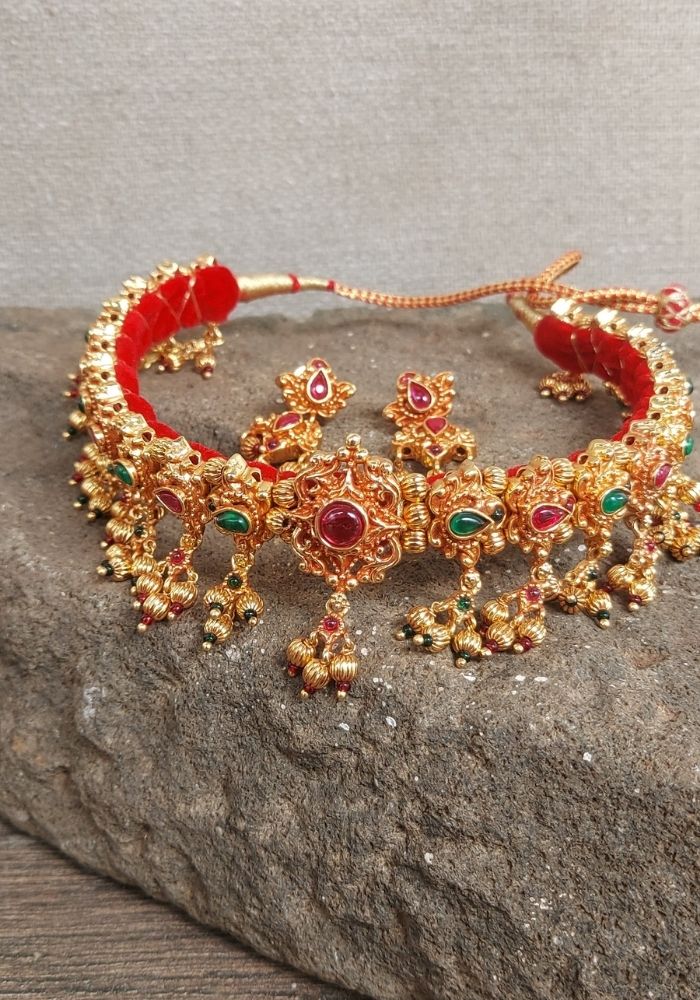 Ornate golden and red antique necklace with intricate floral designs, featuring colorful gemstones on a stone surface