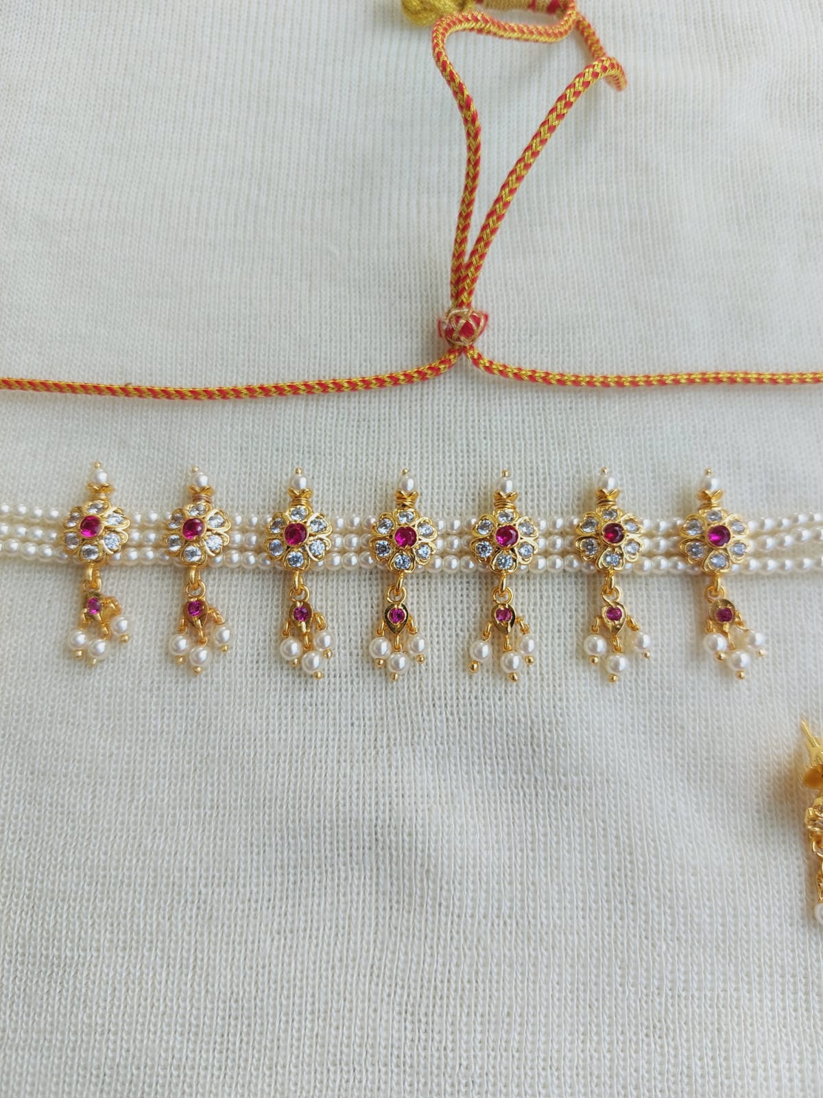 Detailed floral necklace with pearl and ruby embellishments, hanging on a white background.