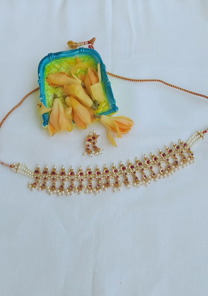 Elegant gold-toned jeweled necklace and earrings alongside a vibrant embroidered clutch bag from Mugdha Jewellery Store.