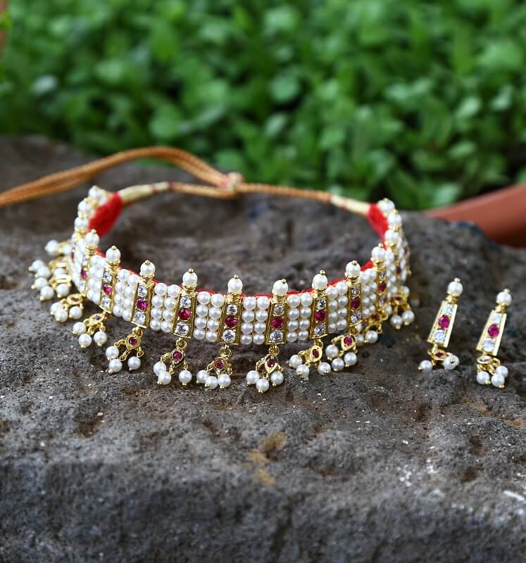 Dark Pink White Stone 4 Patti Gadi Chinchpeti Necklace and Earrings Set
This image shows a Mugdha Jewellery Store product, a dark pink and white stone statement necklace with a multi-row design and matching earrings. The necklace features intricate golden detailing and pearls, creating a luxurious and elegant look.