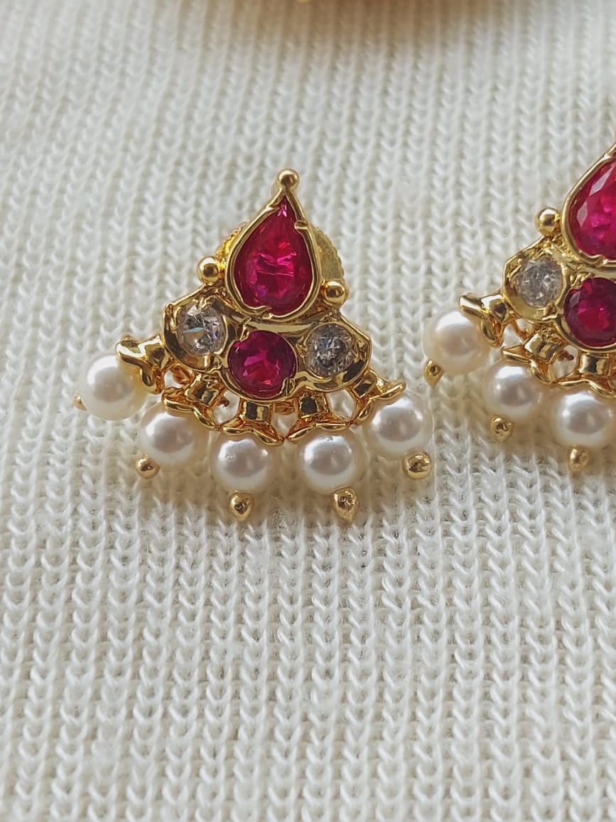 Elegant pearl choker with ruby-colored gems and gold-toned accents displayed on a white knitted surface.