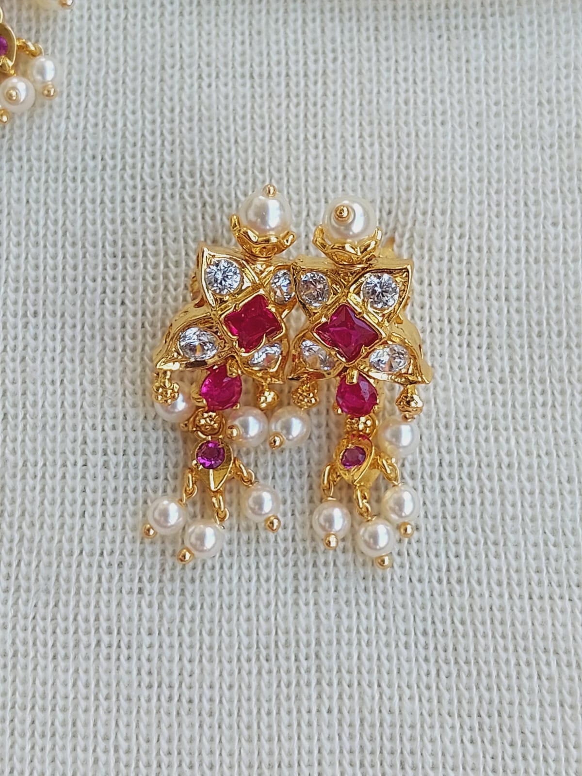 3 Patti Designer Red Flower Chinchpeti, gold-toned floral earrings with red gemstones and pearls, displayed on a white knitted background.