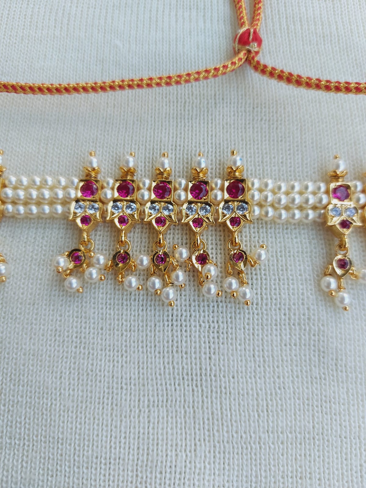 Elegant gold-toned jewelry with intricate ruby and pearl details displayed on a light-colored textile background from Mugdha Jewellery Store.