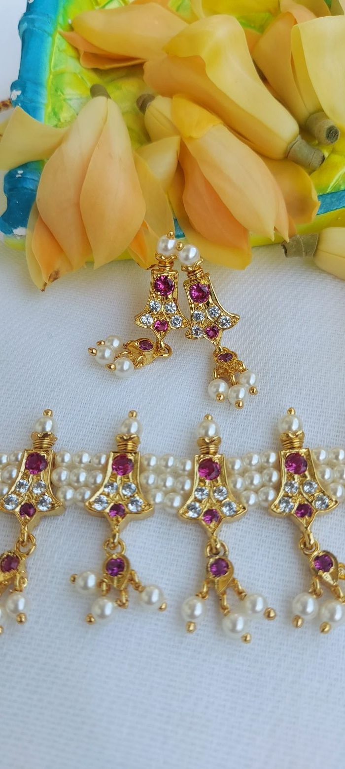 Vibrant gold and gemstone traditional Indian jewelry with pendant and dangling earrings displayed on a colorful fruit backdrop.