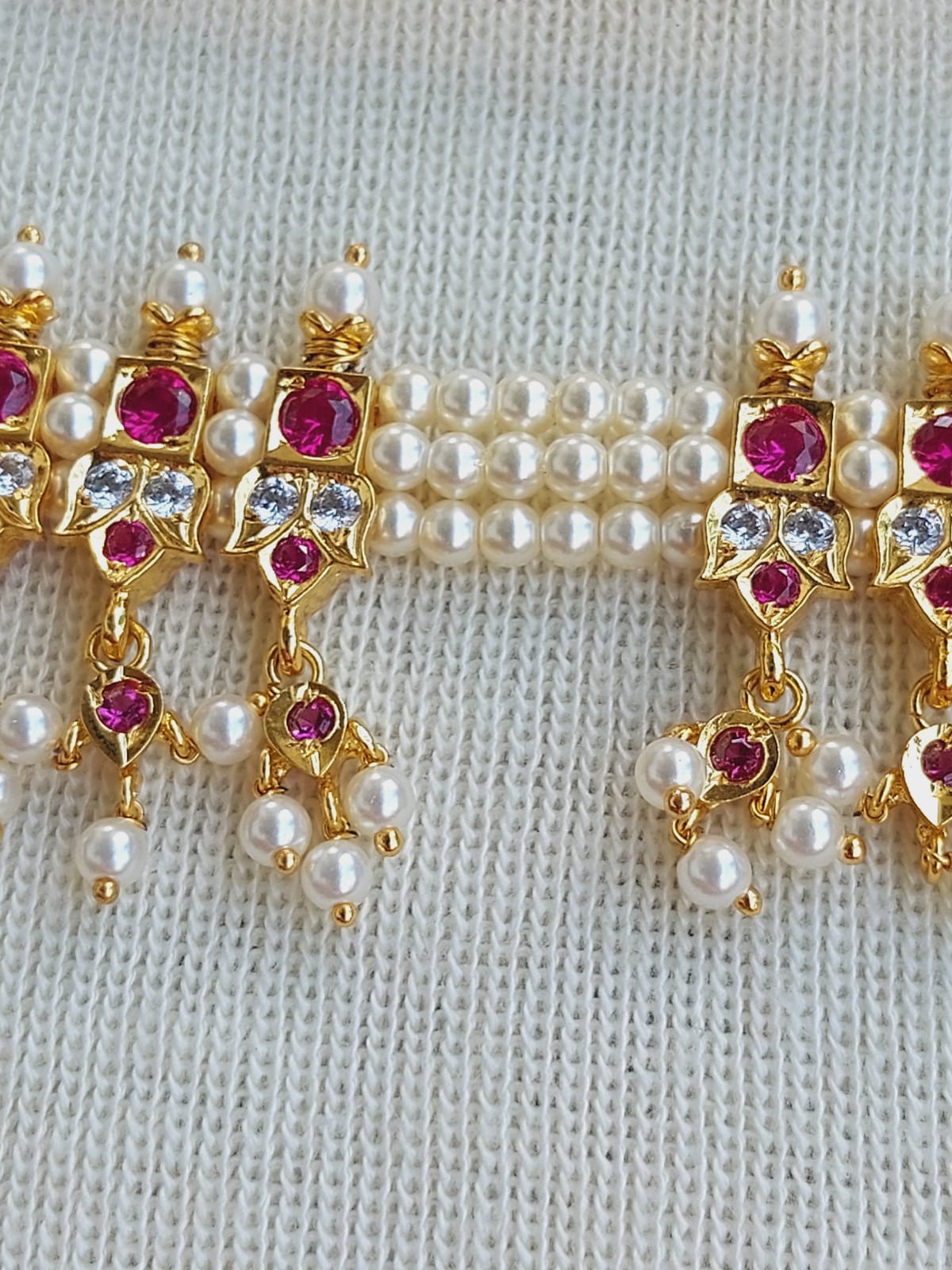 Elegant pearl and ruby embellished gold-tone jewelry pieces, featuring intricate designs and hanging pearl accents, displayed on a knitted fabric background.