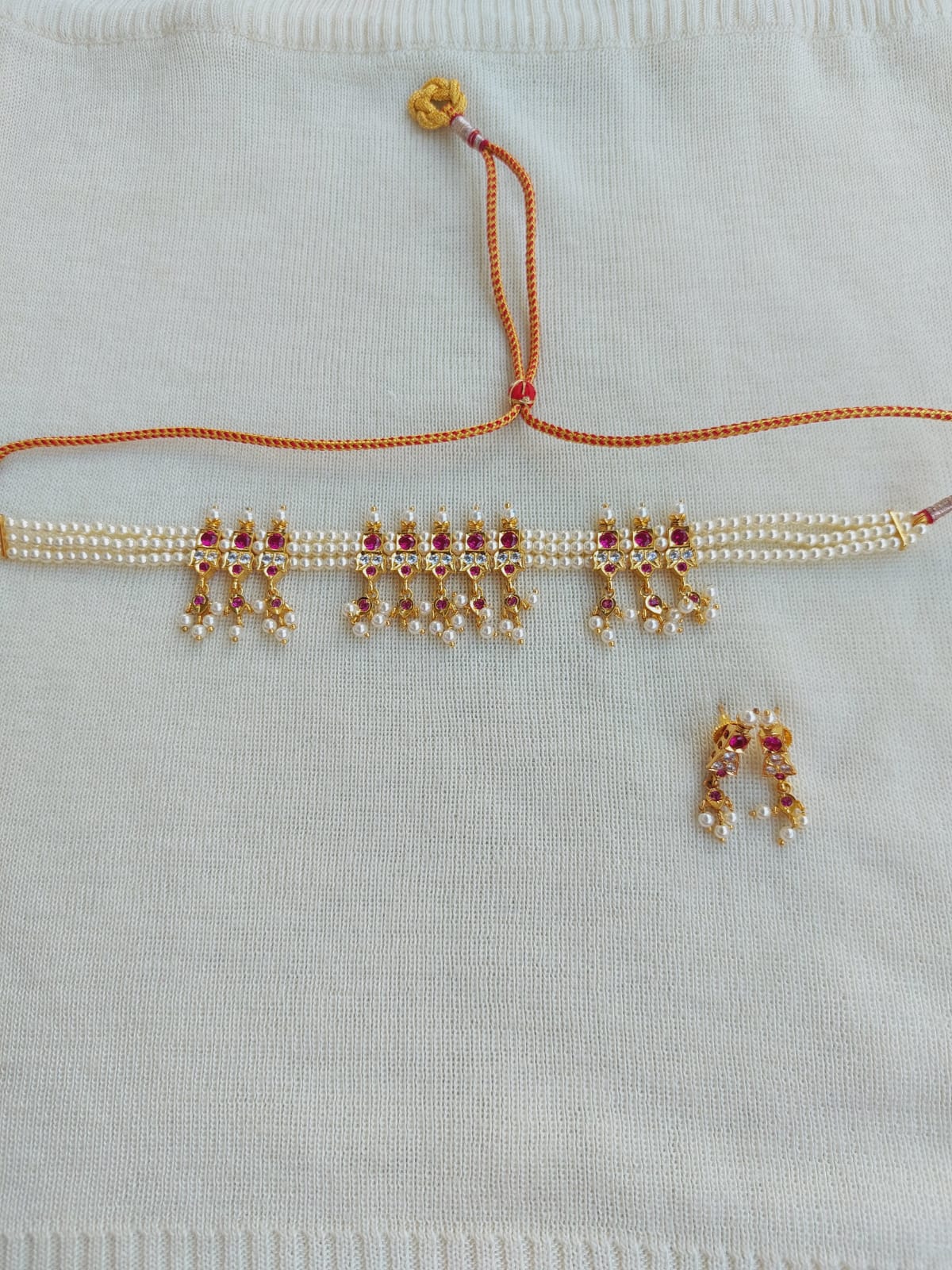 Ornate gold and red traditional Indian jewelry displayed on a white fabric background, featuring a necklace with intricate patterns and a dangling earring set.