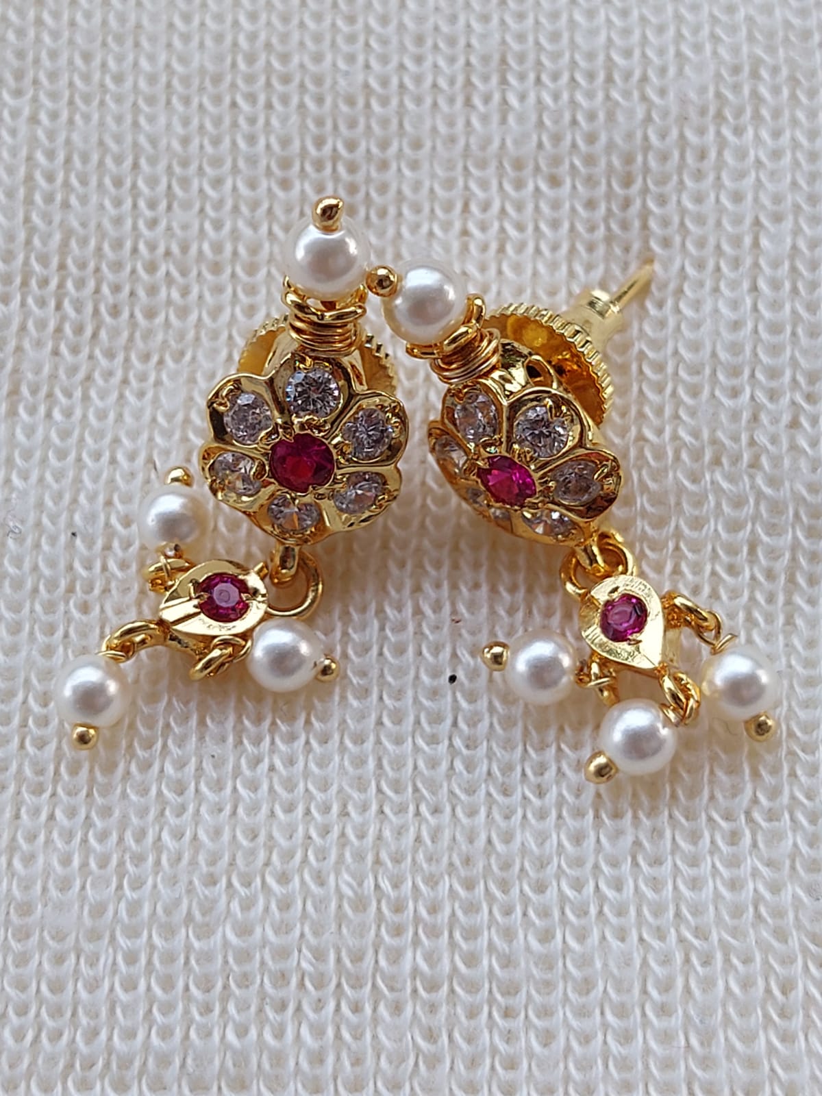 Elegant gold-tone flower earrings with gems and pearls showcased on a textured white fabric background.