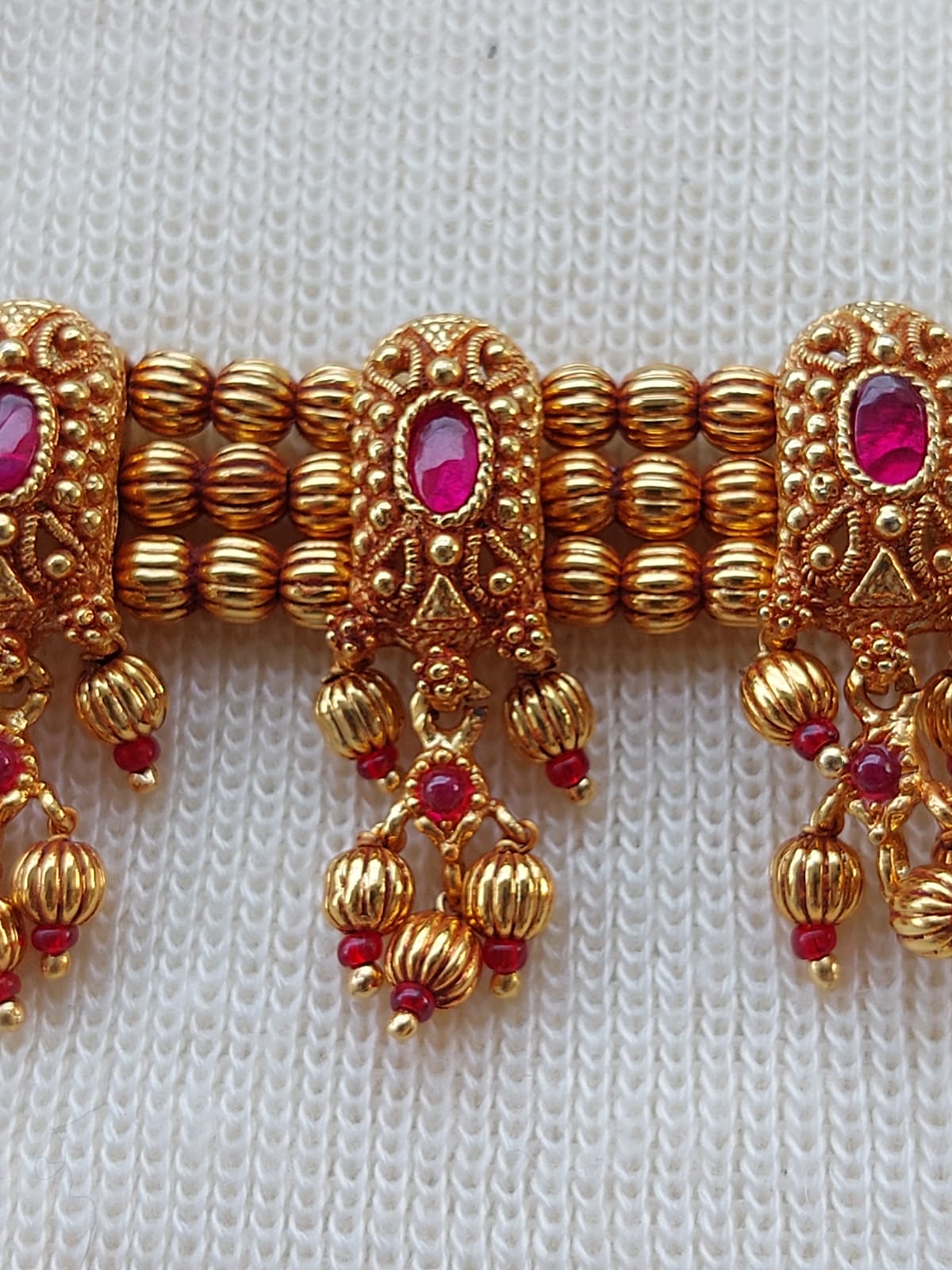 Ornate golden jewelry with intricate patterns and red gemstones, showcased against a plain white background.