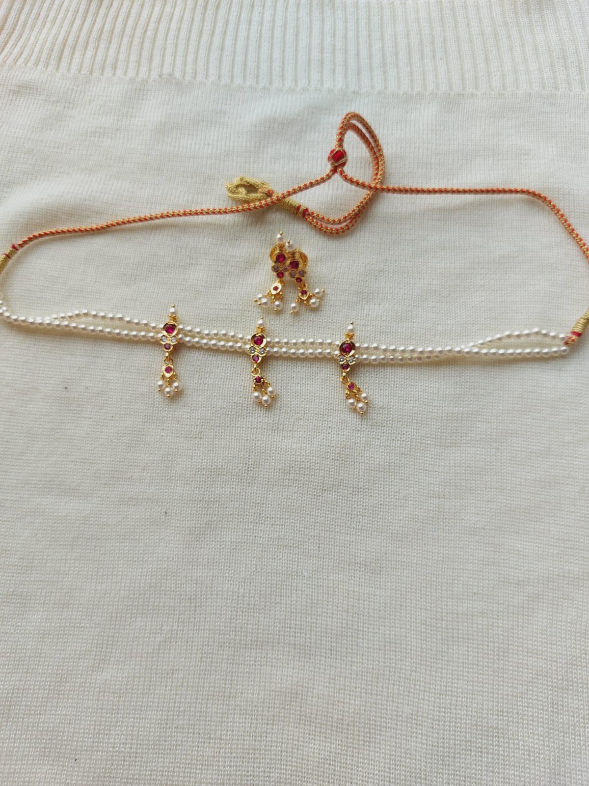 Elegant 3 Patti Small Cute Chinchpeti 2 Necklace from Mugdha Jewellery Store. Delicate golden charms with red stones adorn the adjustable woven cord, creating a beautiful and eye-catching accessory.