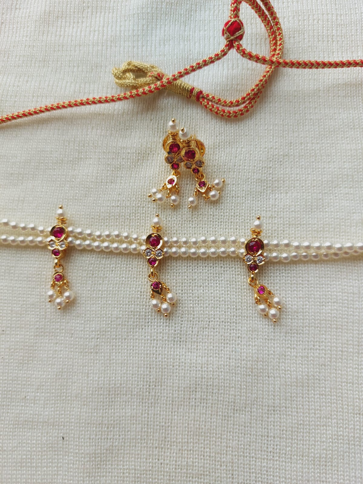 Intricate traditional Indian jewelry pieces showcased on a light background, including a pendant with rubies and pearls, and matching earrings adorned with sparkling gemstones.