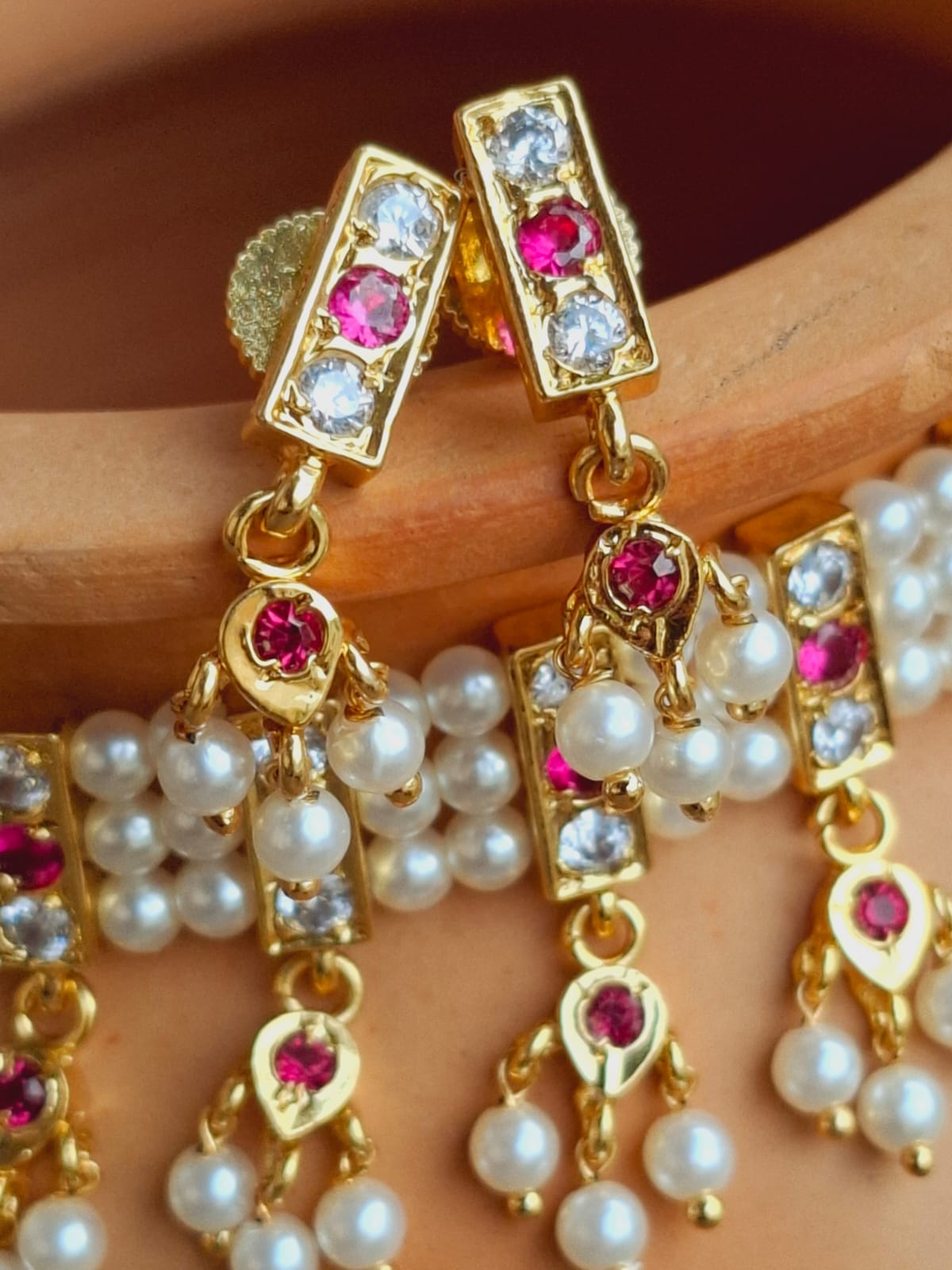 Ornate gold earrings with sparkling gemstones and cascading pearl drops, showcased on a woman's hand.