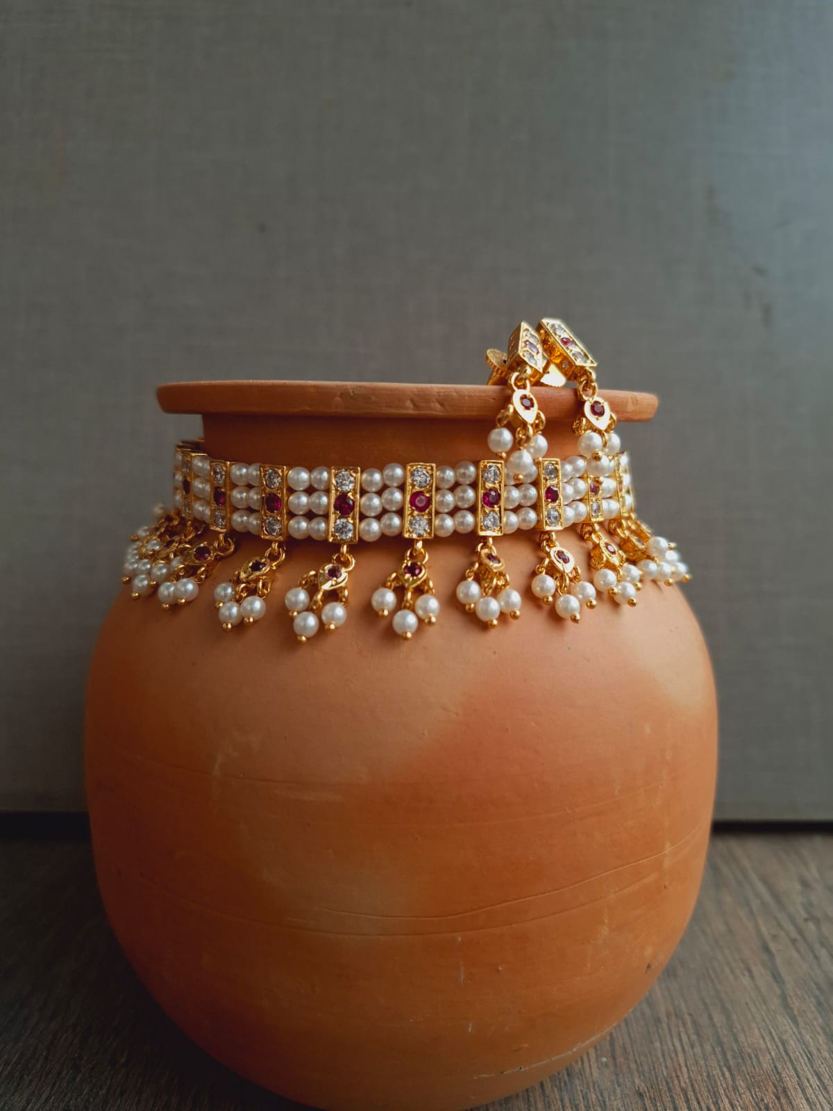 Traditional gold-toned 19-patti chinchpeti necklace with intricate pearl and crystal detailing, displayed on a terracotta pot.