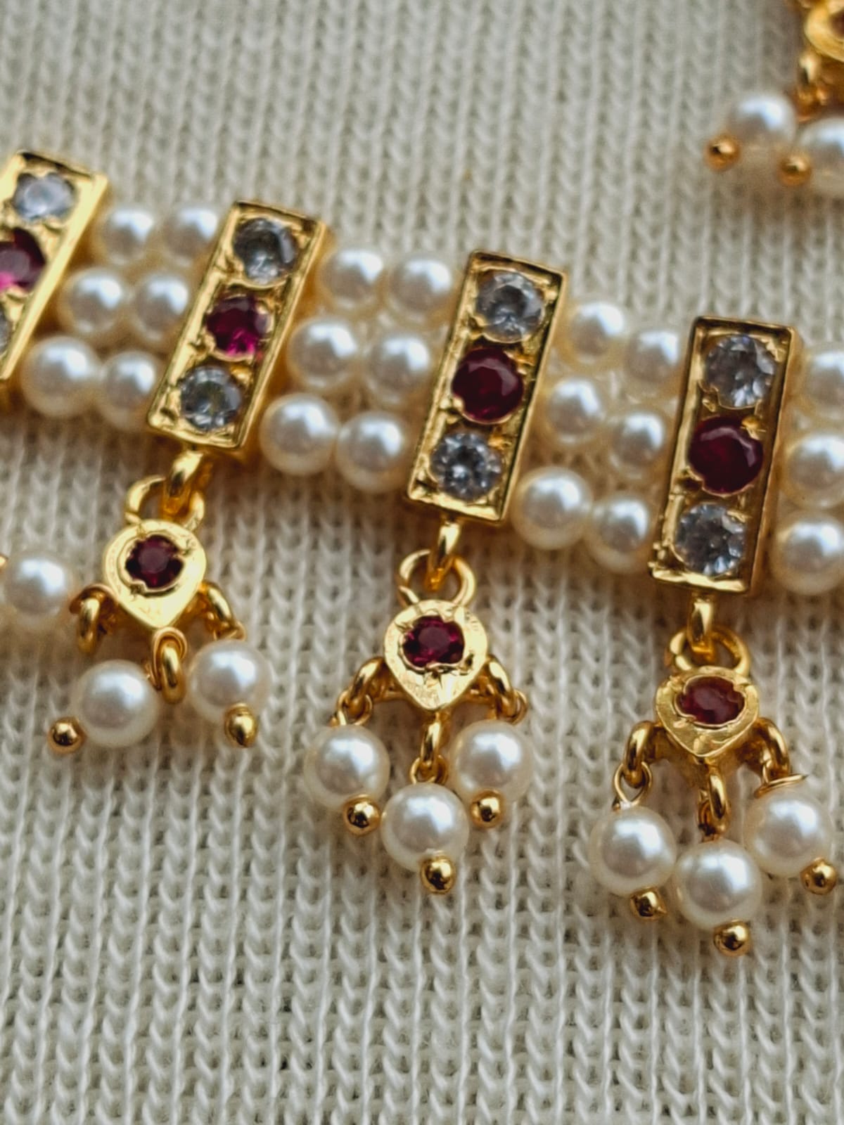 Gold-toned traditional Indian chinchpeti with pearl and ruby accents displayed on a knitted fabric background.