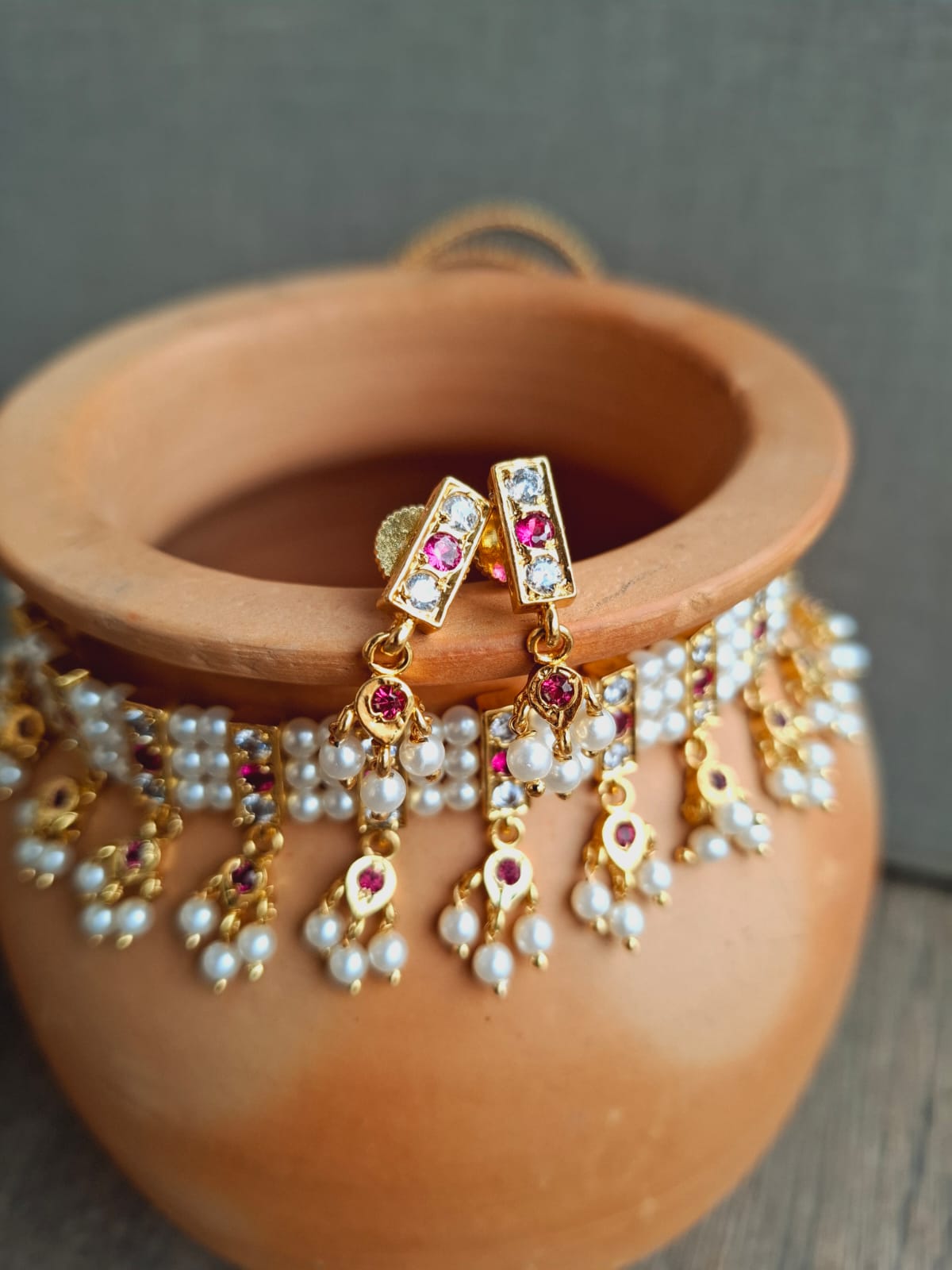 Ornate gold and pearl traditional Indian earrings displayed in a terracotta pot