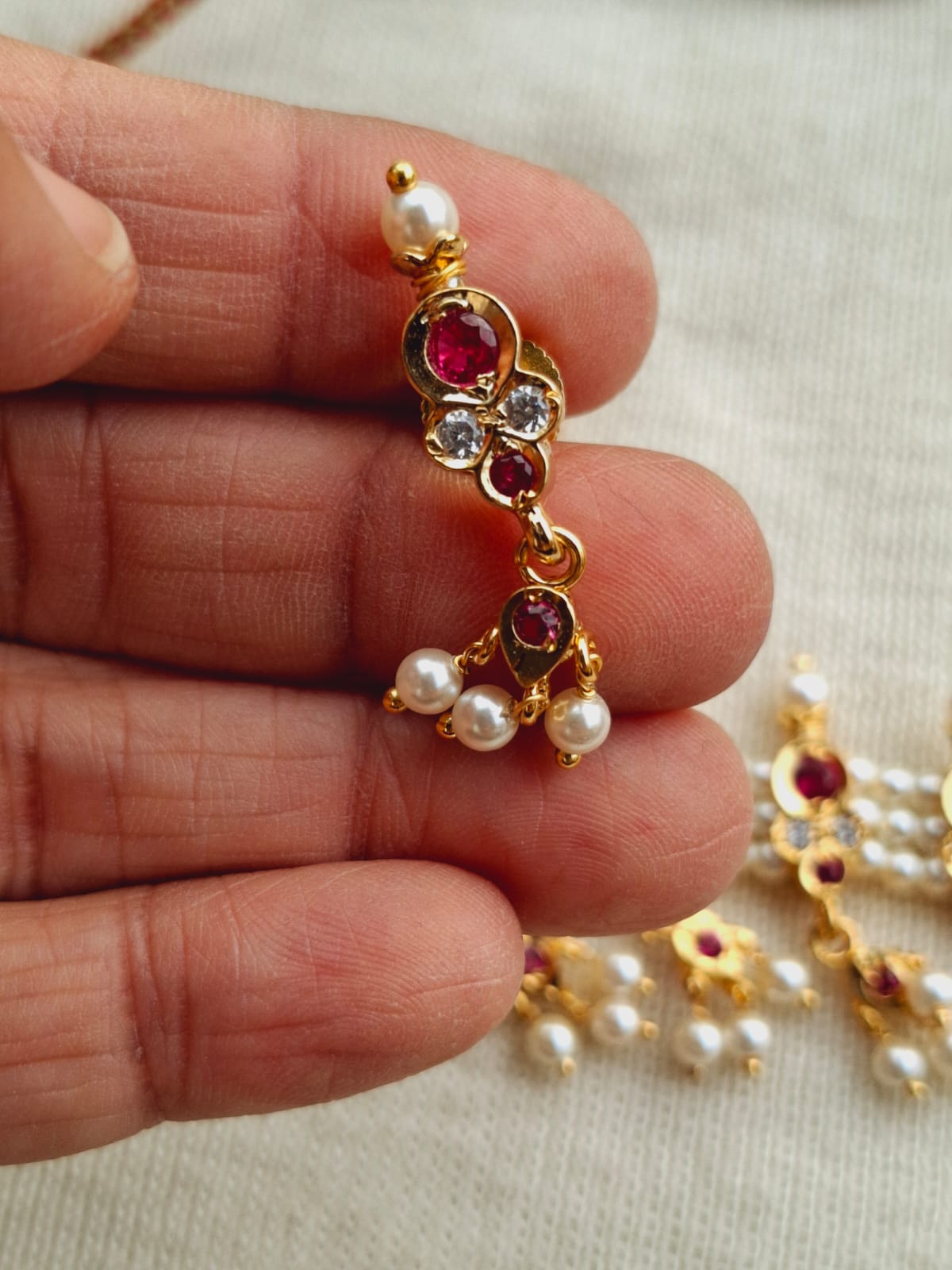 Elegant gold-toned earring with ruby gems and pearls, showcasing intricate jewelry craftsmanship.