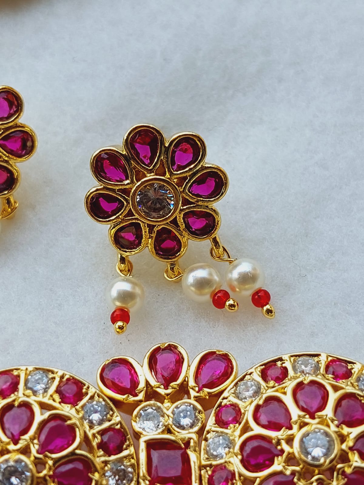 Elegant gold-toned choker with intricate floral design and vibrant pink gemstones, accented with delicate pearls and subtle sparkles, showcased on a plain background.