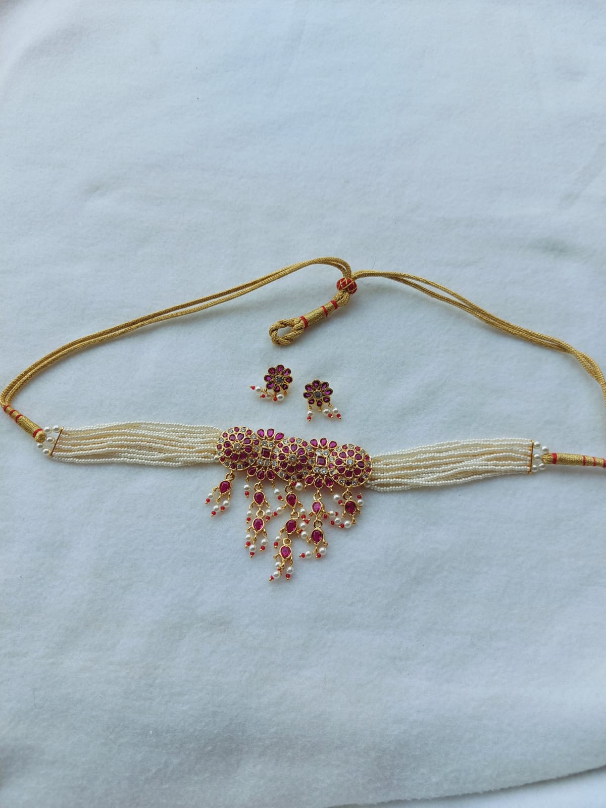 Elegant gold-toned choker necklace embellished with sparkling ruby-colored gems, accompanied by matching stud earrings, showcased on a plain background.