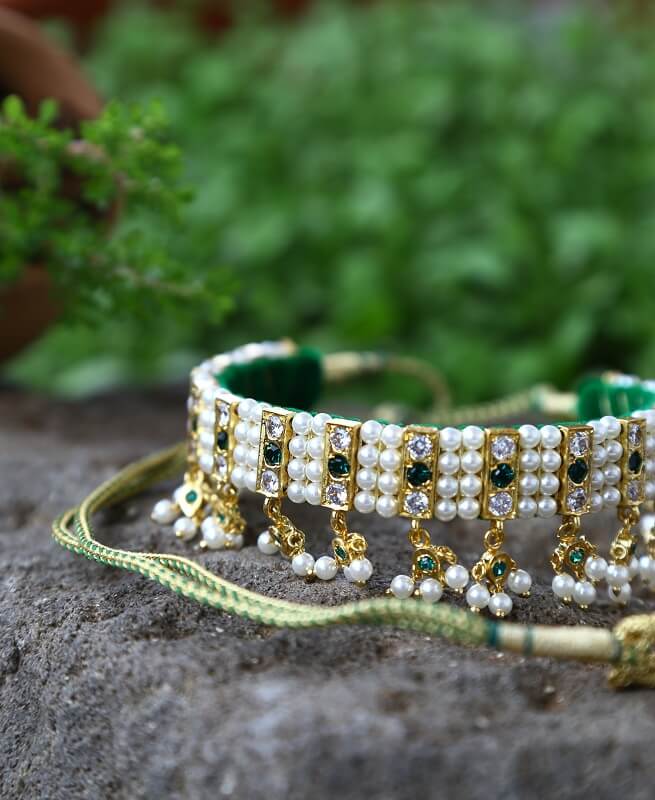 Ornate green and gold beaded necklace with sparkling gemstones and pearls, displayed on a rocky surface against a blurred natural green backdrop.