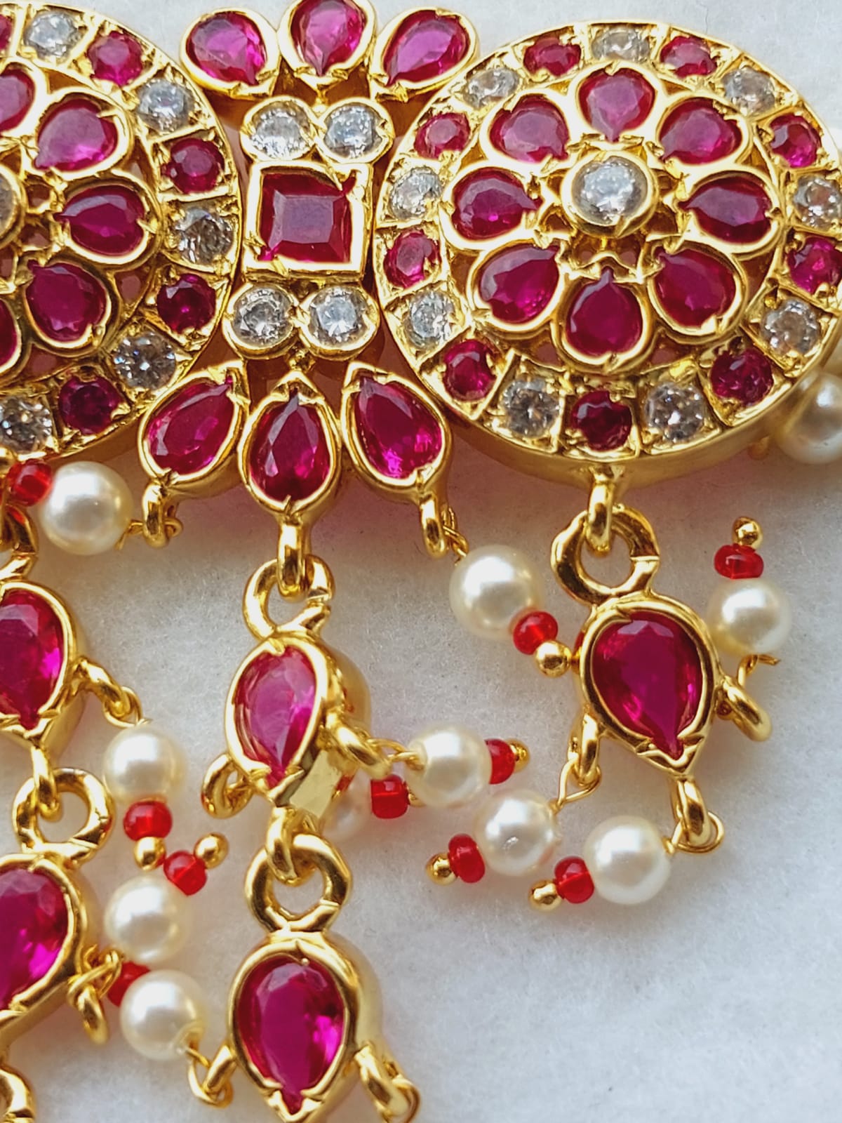 Exquisite gold-toned necklace with vibrant ruby-colored gemstones and shimmering pearls, showcasing intricate floral-inspired design.