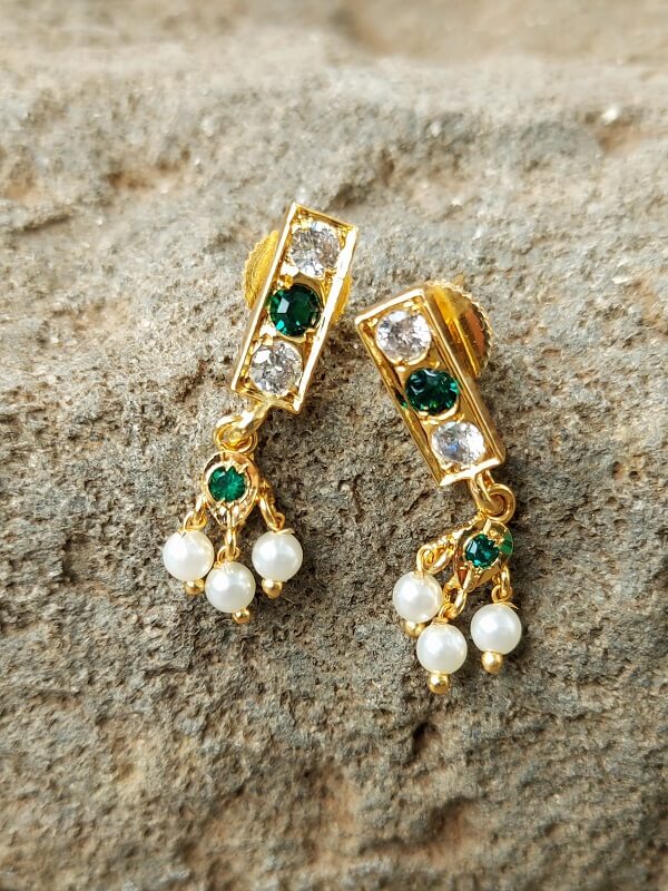 Elegant green and white stone earrings with pearl accents, set in a gold-tone metal frame, displayed on a textured beige surface.
