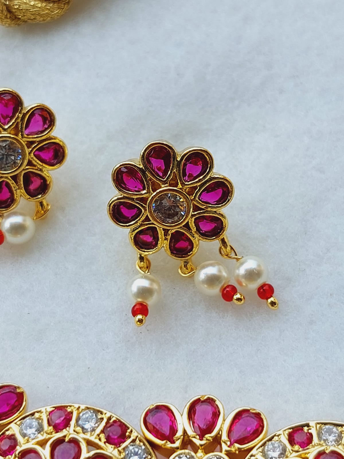 Exquisite floral-shaped gold choker studded with vibrant ruby-colored gemstones and accented with delicate pearl drops, showcased elegantly against a plain white background.