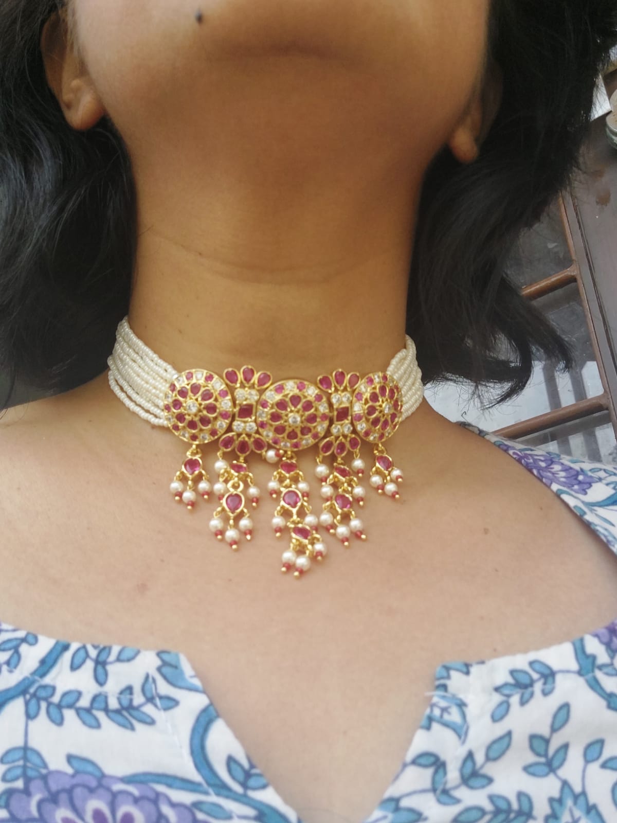 Elegant ruby and pearl necklace displayed on woman's neck against floral patterned background in Mugdha Jewellery Store.