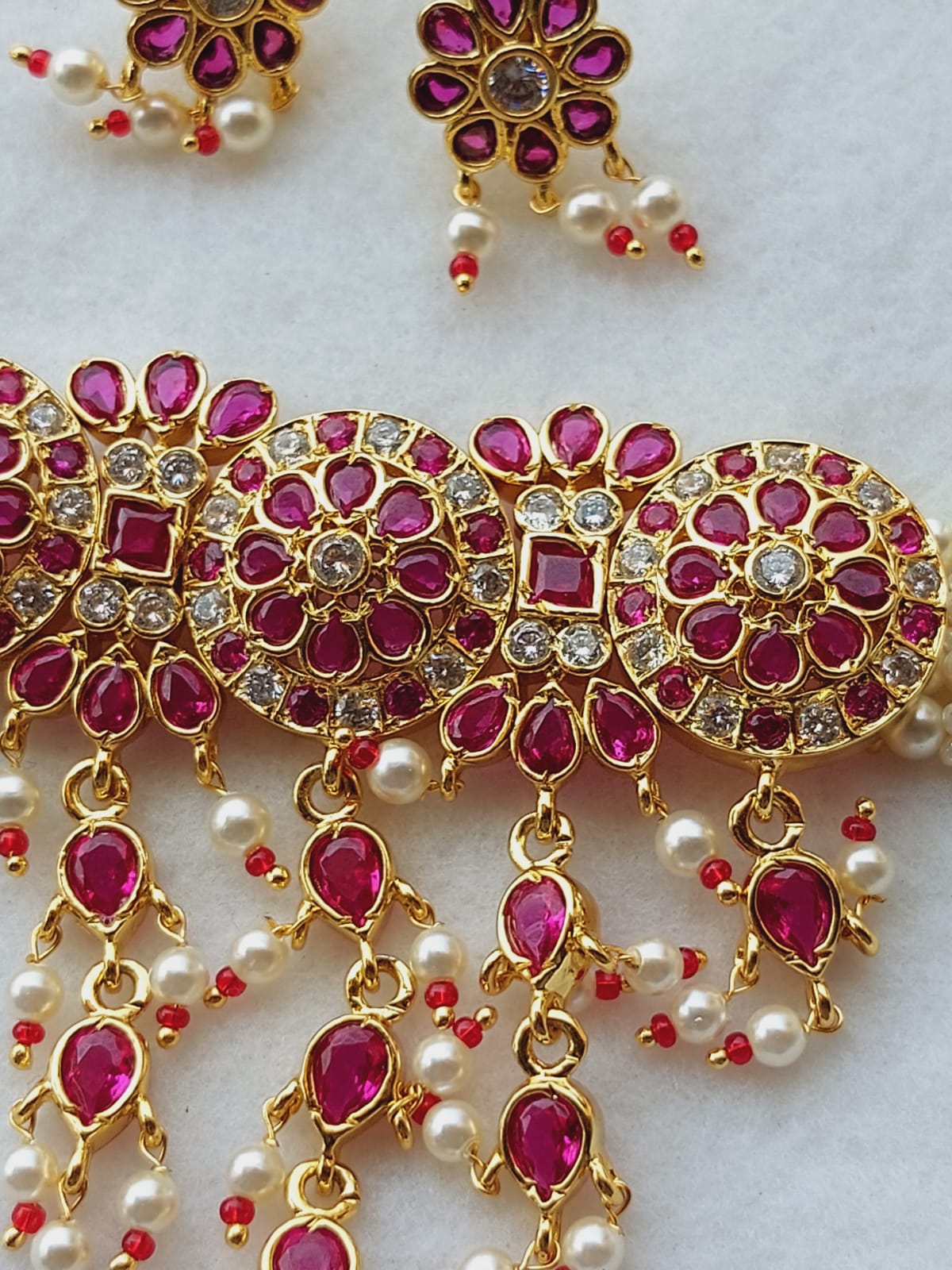 Ornate gold and ruby jewelry with intricate flower and teardrop designs, featuring sparkling gemstones and hanging pearls.