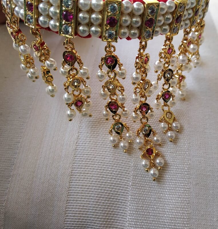 Ornate gold and pearl necklace with intricate beaded detailing and hanging ruby-colored gemstone accents.