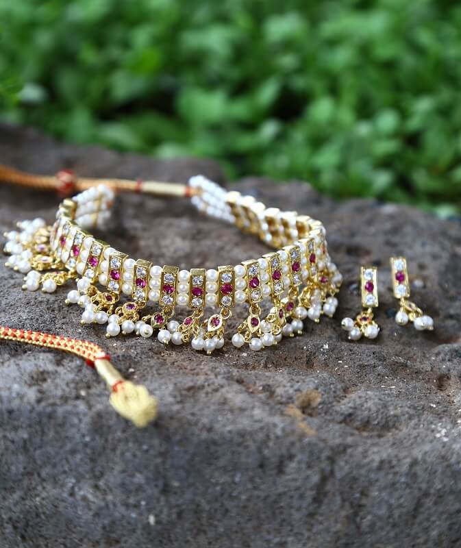 Elegant pearl necklace and earrings set with intricate floral design, adorned with vibrant gems against lush natural backdrop.