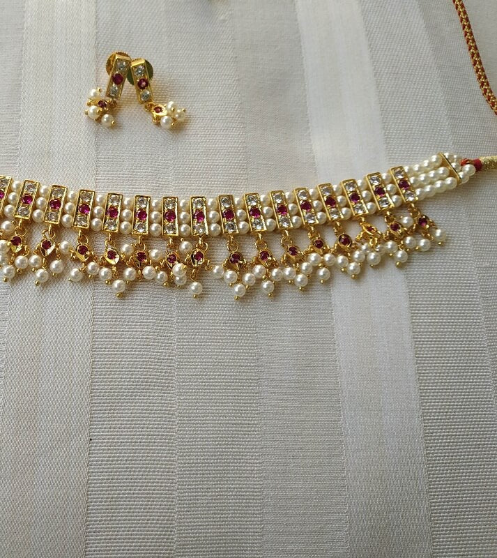 Elegant gold-toned pearl and crystal choker necklace with intricate beading and dangling pendants, showcasing fine craftsmanship from the Mugdha Jewellery Store.