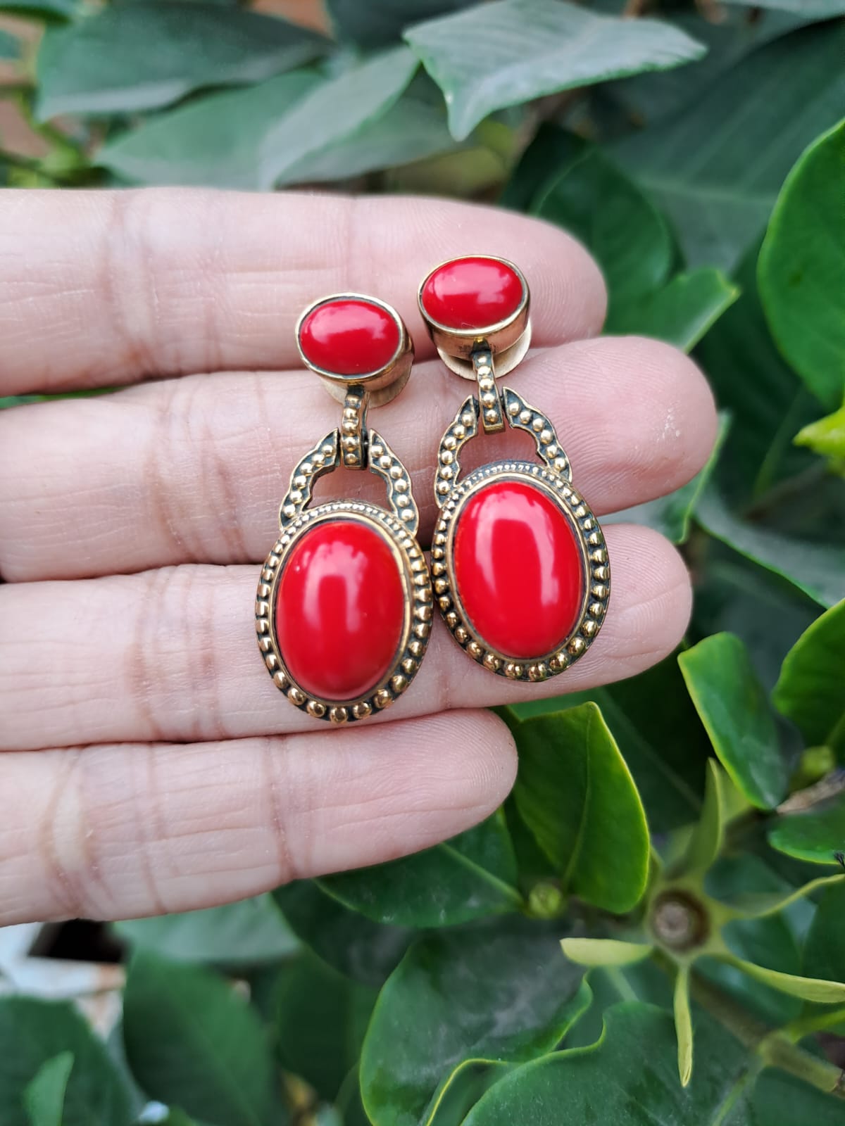 Elegant Red Stone Dangler Earrings - High-quality gold-tone earrings with vibrant red stones, displayed against a lush green foliage background.