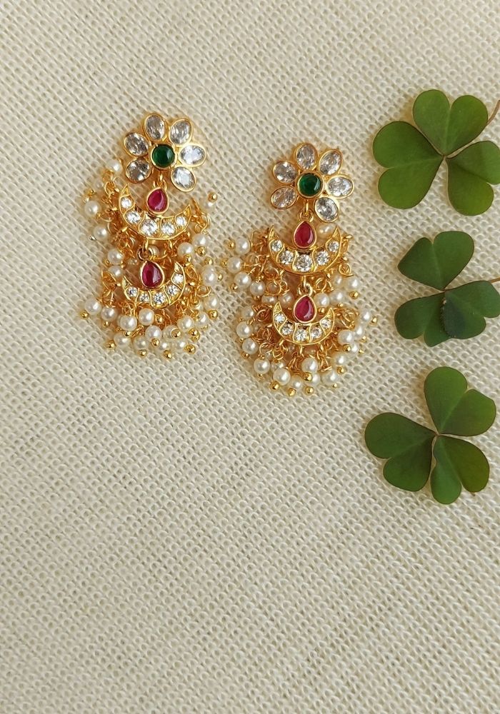 Elegant multicolored rice pearl earrings with floral motif, surrounded by green shamrock leaves on a light background.