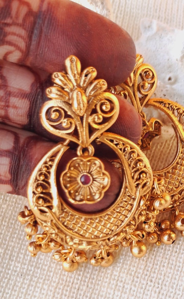 Elegant gold dangler earrings with intricate floral and swirl designs, showcased on a textured fabric surface.