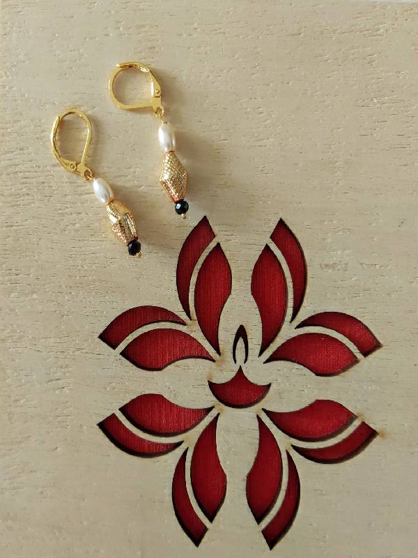 Elegant pearl and gold dangler earrings set against a textured light background with a red floral design.
