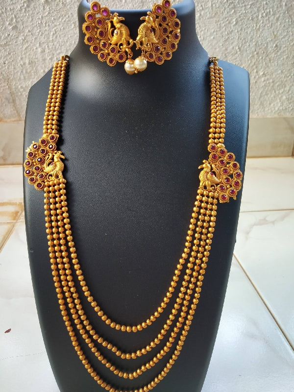 Elegant gold-toned peacock pendant and multi-strand necklace set from Mugdha Jewellery Store featuring intricate floral designs and vibrant red gemstones.