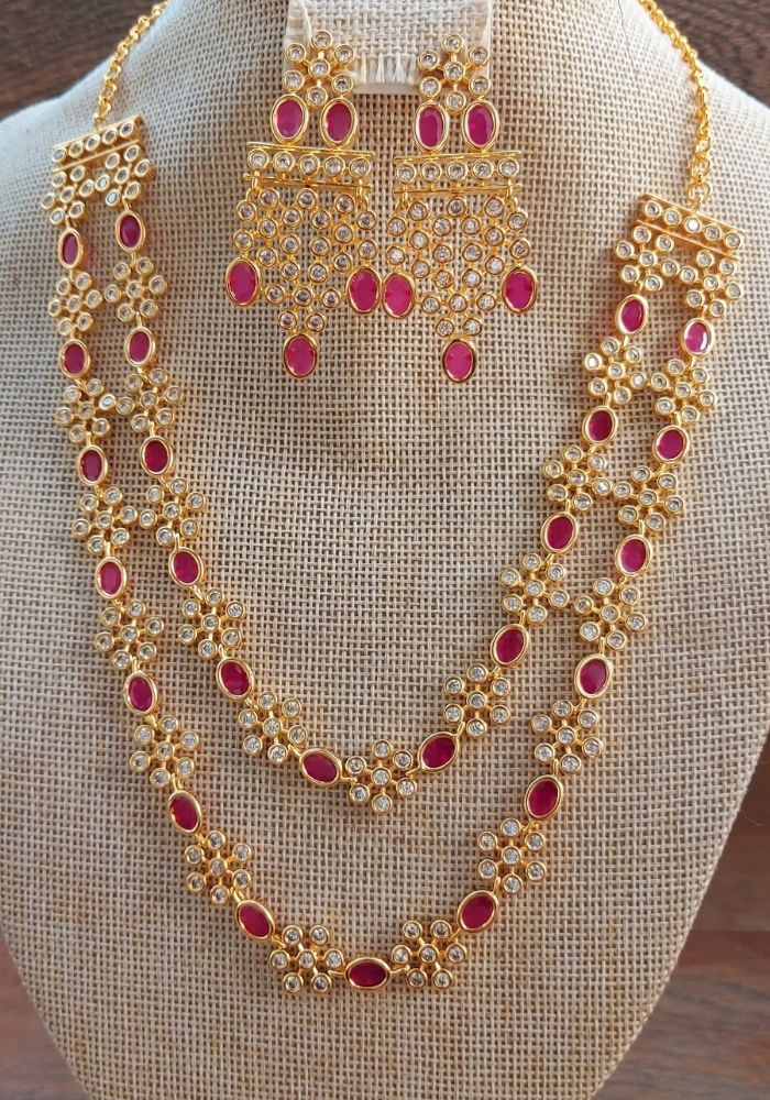 Elegant gold jewelry set with intricate design featuring ruby-colored stones and floral patterns, placed on a beige fabric background.