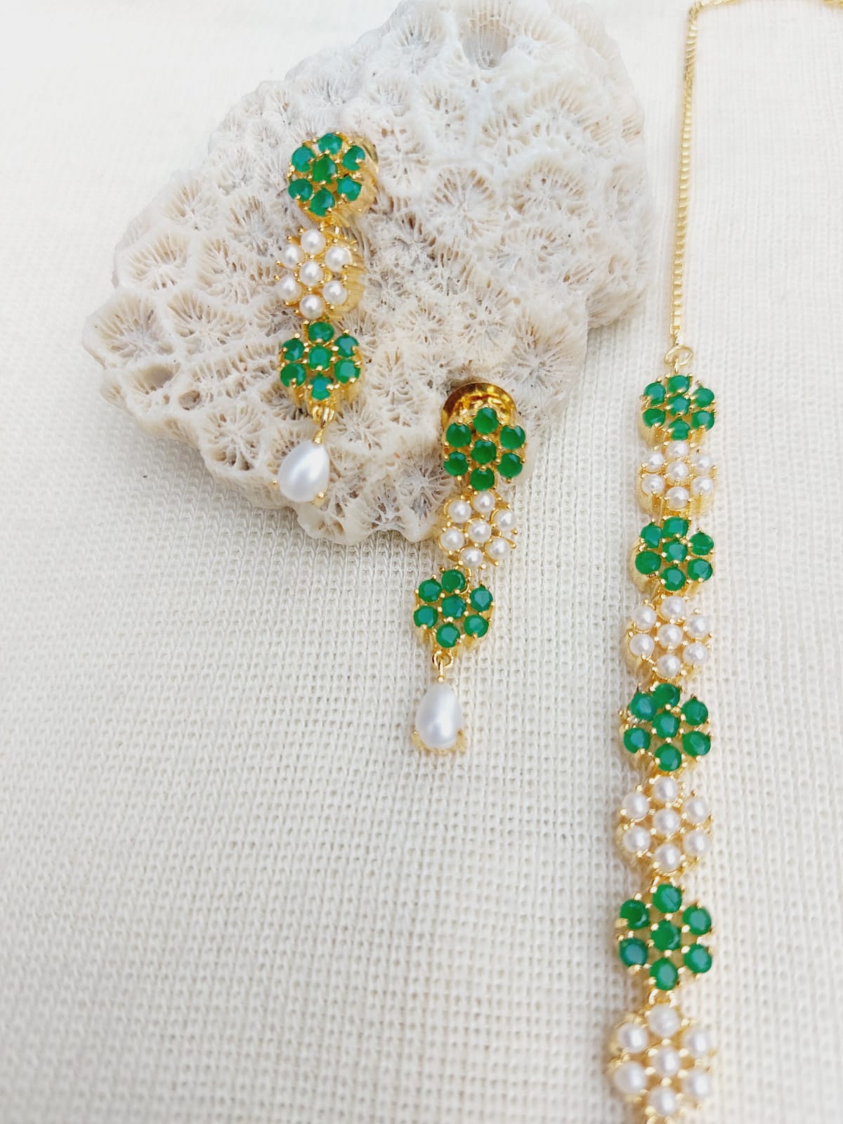 Elegant green stone and pearl floral necklace and earring set on a soft white fabric background.