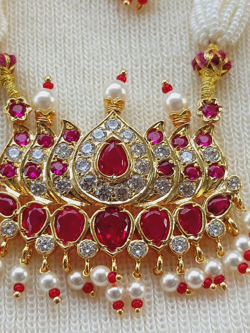 Ornate gold-toned designer pendant with embedded red gemstones and pearls, showcased on a white knitted background.