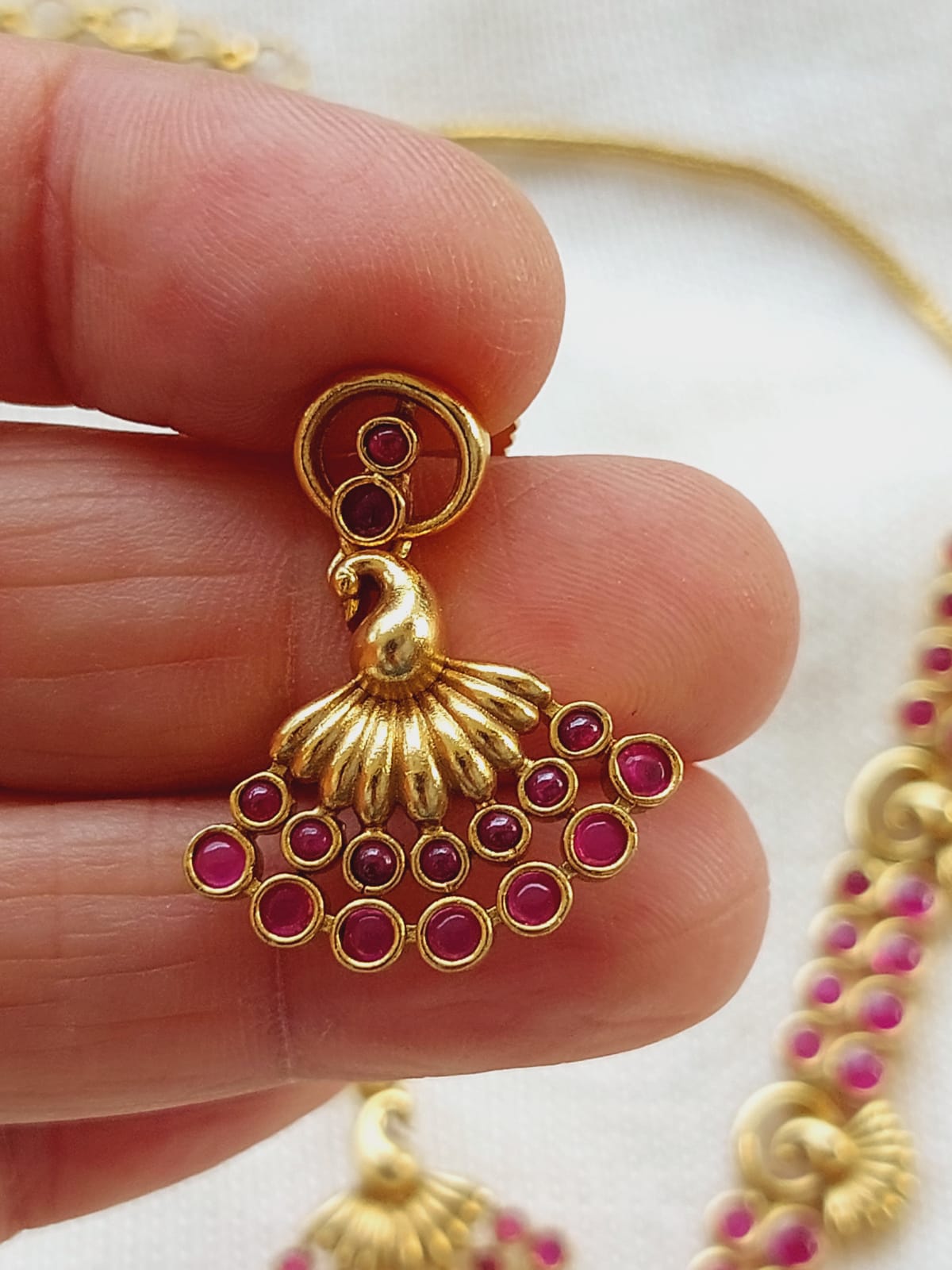 Elegant gold-toned peacock-shaped pendant with glittering ruby-colored stones, showcased in a close-up image against a white background.