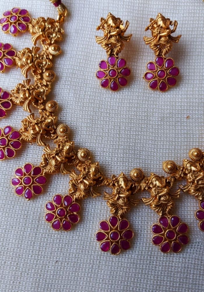 Ganesha Designer Necklace - Ornate gold-tone necklace with intricate floral designs and vibrant ruby-colored accents, showcased on a plain light-colored background.