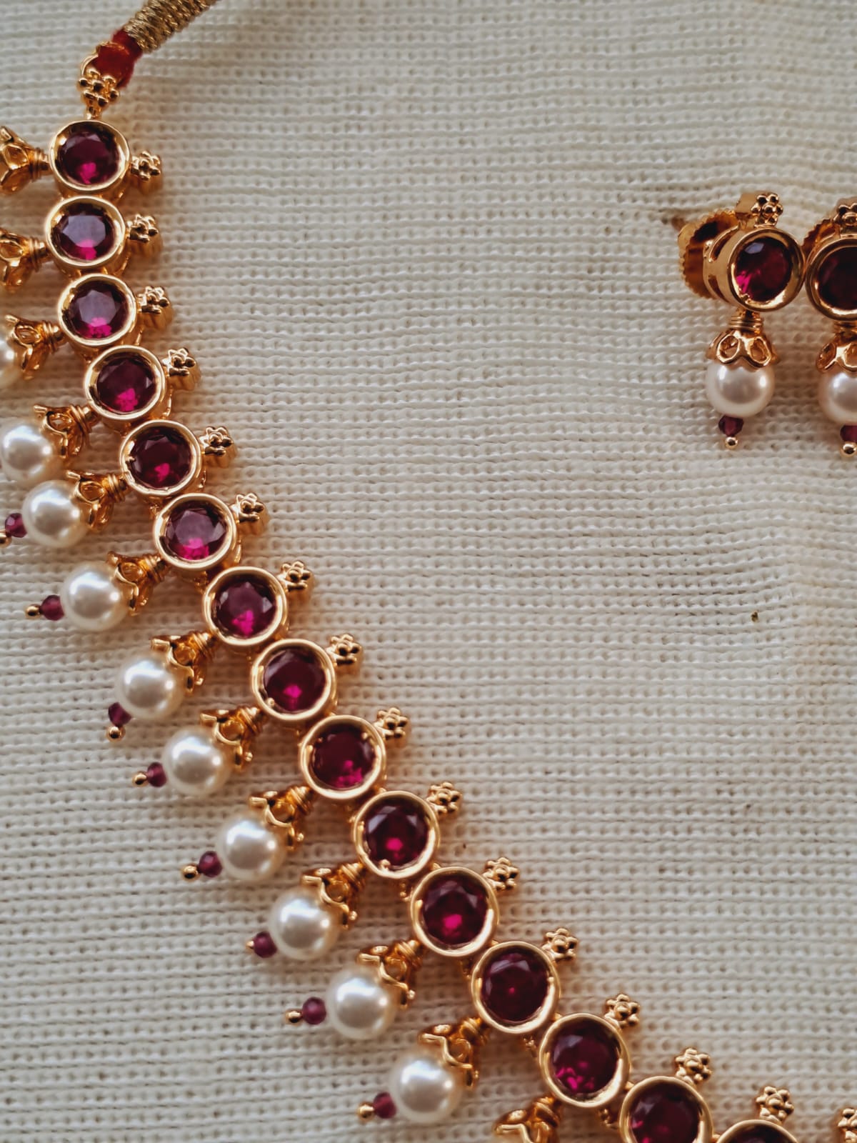 Elegant gold necklace adorned with dark pink stones and delicate pearl accents, presented on a simple white background.