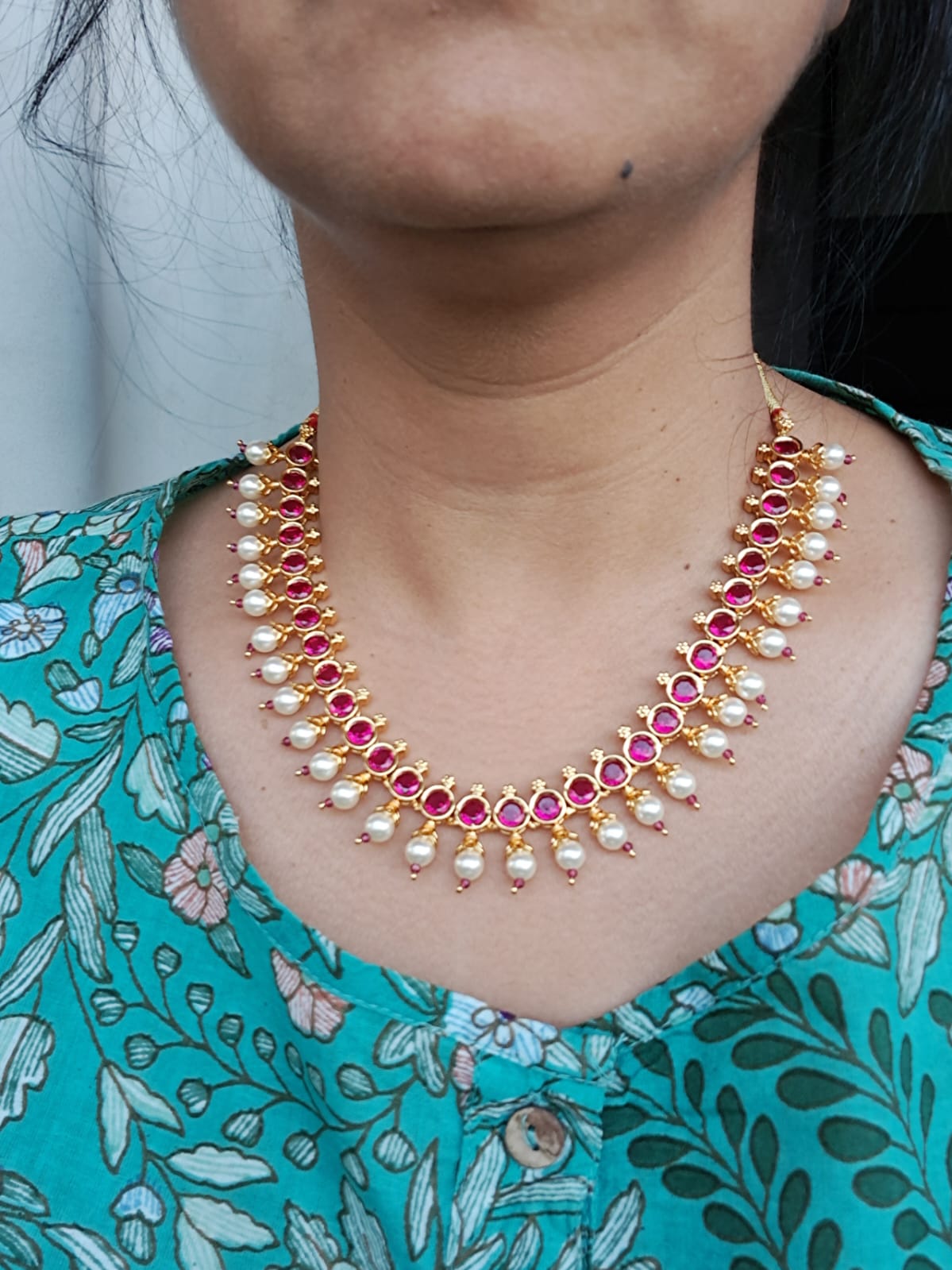 Elegant pink stone necklace with pearls on model's neck against floral patterned dress