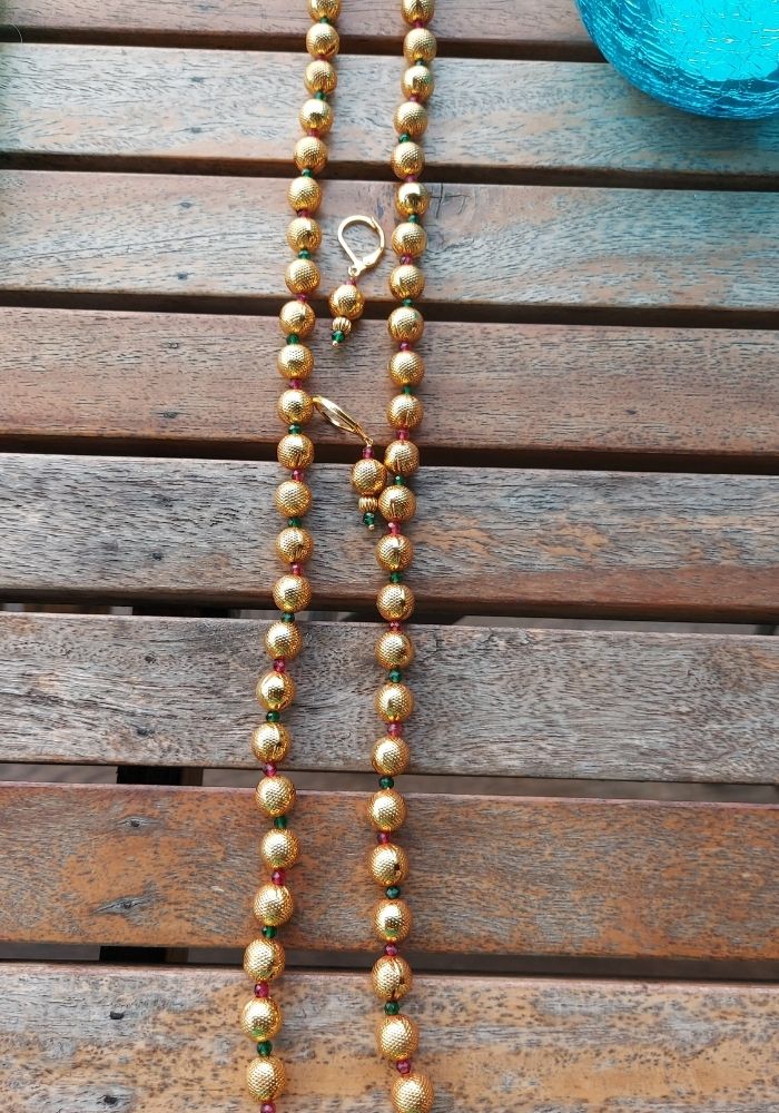 Elegant gold-toned beaded necklace with a lyre-shaped pendant on a wooden background