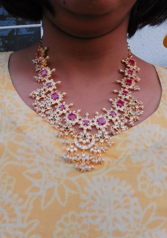 Stunning floral necklace with vibrant pink and white gemstones, worn over a yellow patterned blouse.