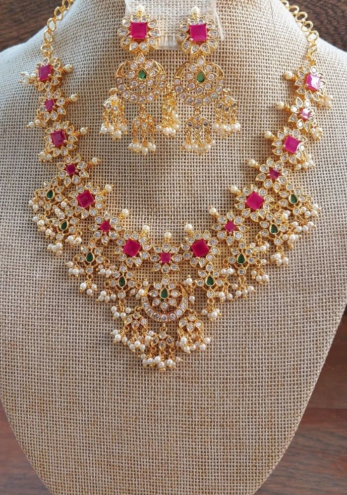 Elegant gold and ruby floral necklace and earrings set displayed on a beige fabric background.