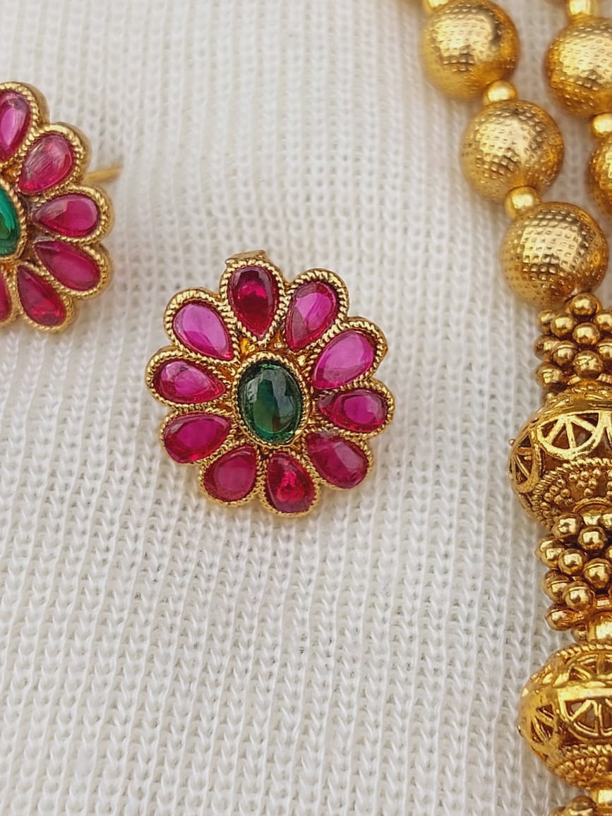 Lavanya Designer Beads Flower Pendant Necklace, vibrant ruby red petal flowers with emerald green accents, set in gold-toned metal frames, displayed on a light-colored fabric background.