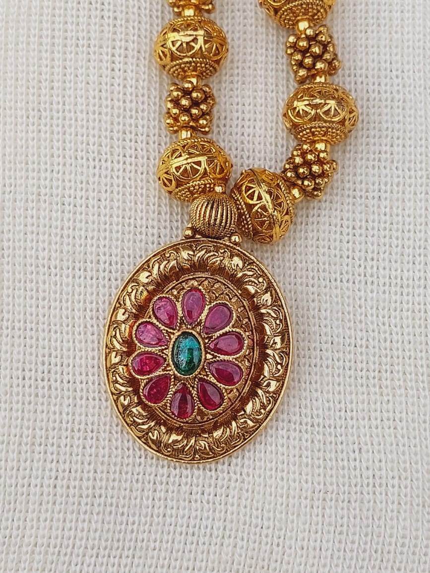Elegant gold-toned floral pendant necklace with intricate beaded design, featuring a vibrant gemstone-encrusted centerpiece on a textured golden chain from the Mugdha Jewellery Store.