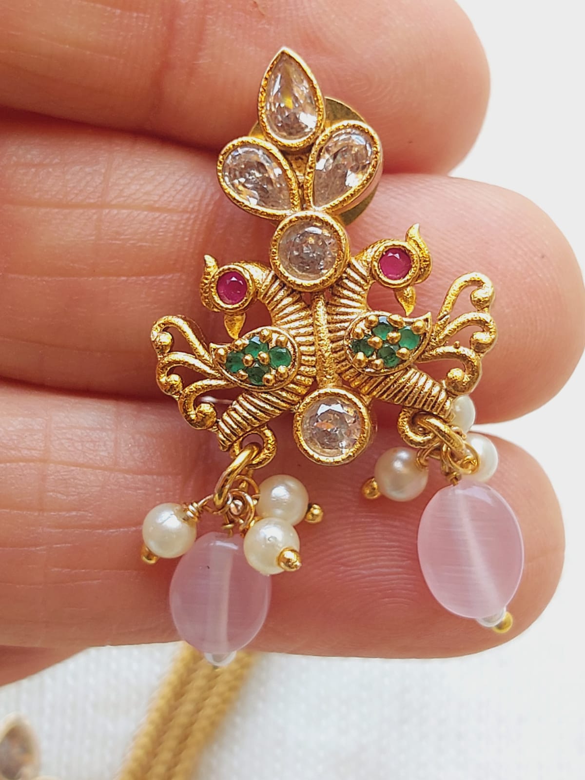 Ornate golden peacock-shaped jewelry piece adorned with kundan stones, baby pink beads, and pearls, displayed on a human hand.