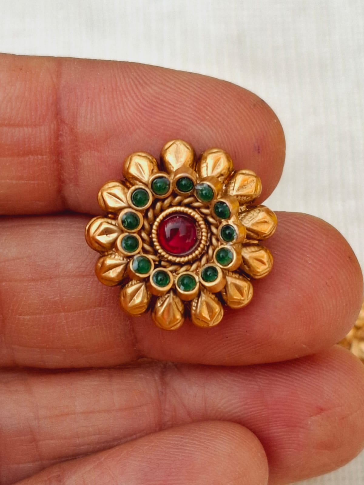 Ornate golden floral pendant with vibrant red and green gemstones showcased in a hand.