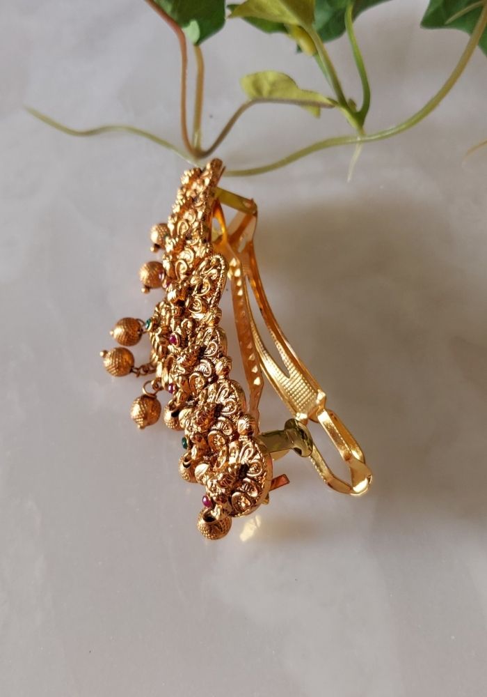 Elegant gold-toned designer hair accessory from Mugdha Jewellery Store, featuring intricate floral patterns and dangling ornaments.